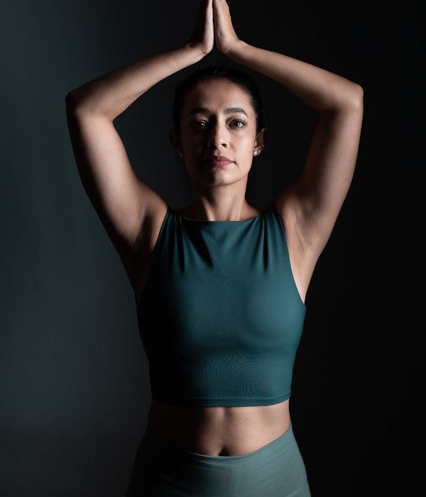 Woman in a calm yoga pose in a dark studio with light blue highlights.
